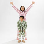 Two children wearing striped robes, one in pink and one in green, standing on a white background.