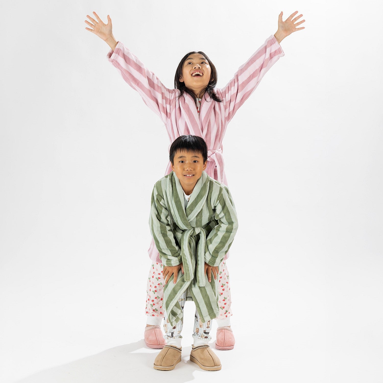 Two children wearing striped robes, one in pink and one in green, standing on a white background.