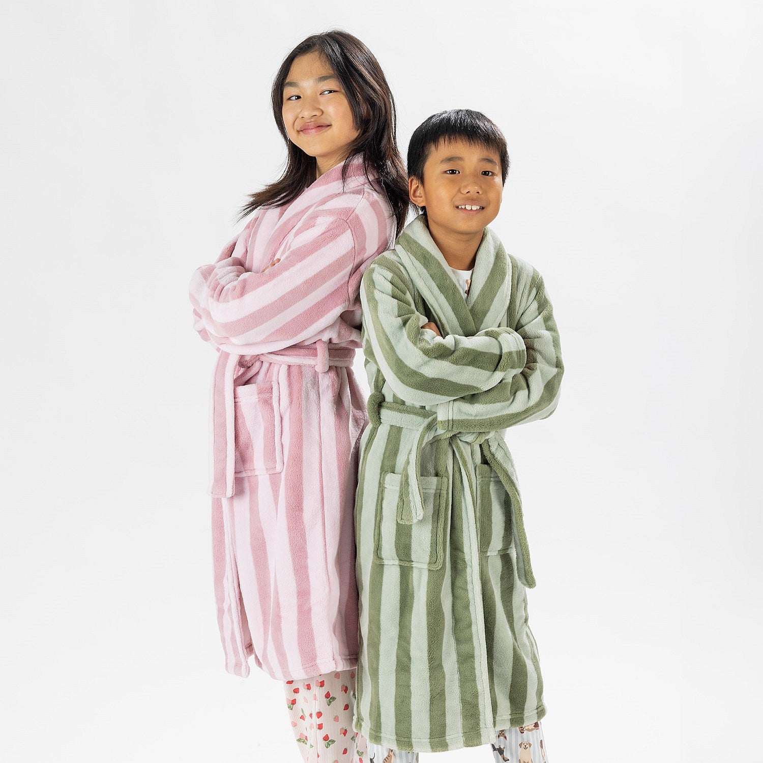 Two children wearing striped robes, one in pink and one in green, standing on a white background.