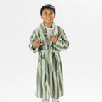 Child wearing a green striped robe standing on a white background.