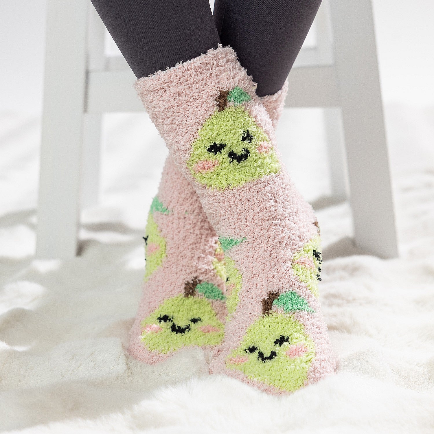 Pink kids bed socks with green pear design, worn on a soft white rug.
