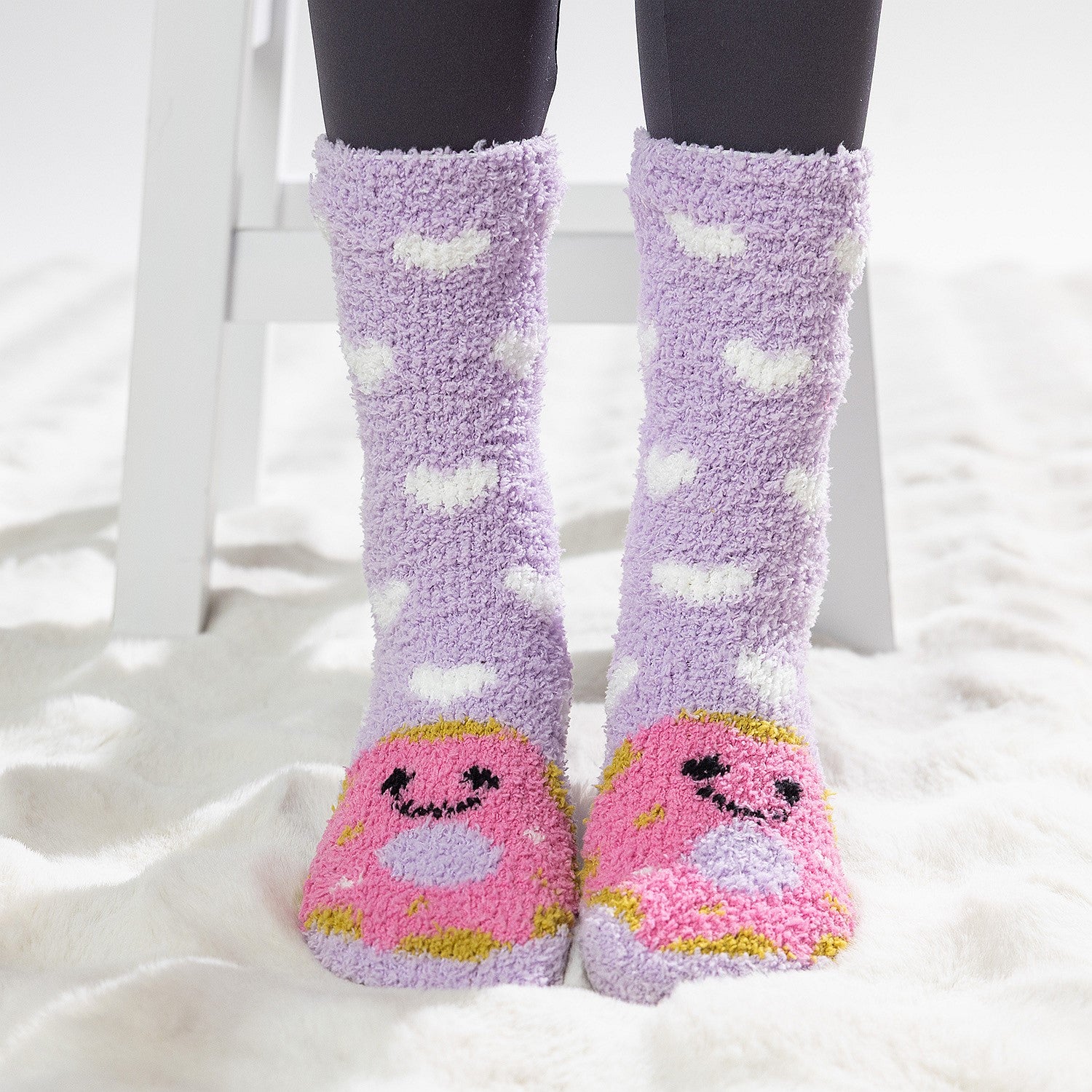 Purple kids bed socks with pink donuts with face design, worn on a soft white rug.