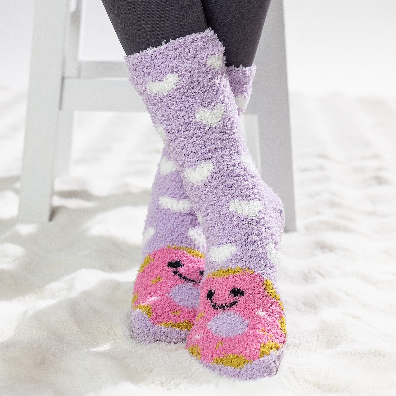 Purple kids bed socks with pink donuts with face design, worn on a soft white rug.