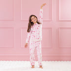 Child wearing pink heart print pyjamas standing against a pink panelled background.