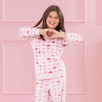 Child wearing pink heart print pyjamas standing against a pink panelled background.