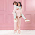 children and adult wearing cosy pyjamas, piggy backing against a pink background.