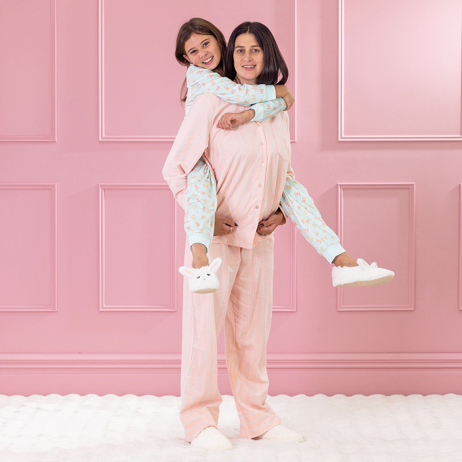 children and adult wearing cosy pyjamas, piggy backing against a pink background.