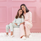 children and adult wearing cosy pyjamas, sitting together on a white ottoman against a pink background.