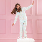 Child wearing light green teddy printed pyjamas standing on a white ottoman against a pink background.