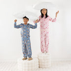 Two children wearing printed pyjama sets, one blue and one pink, standing together on a white rug.