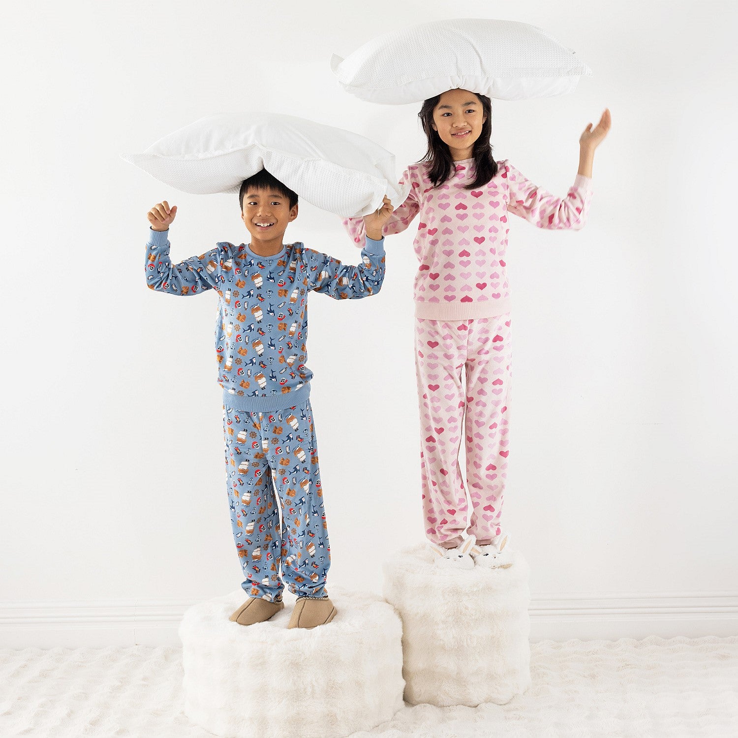 Two children wearing printed pyjama sets, one blue and one pink, standing together on a white rug.