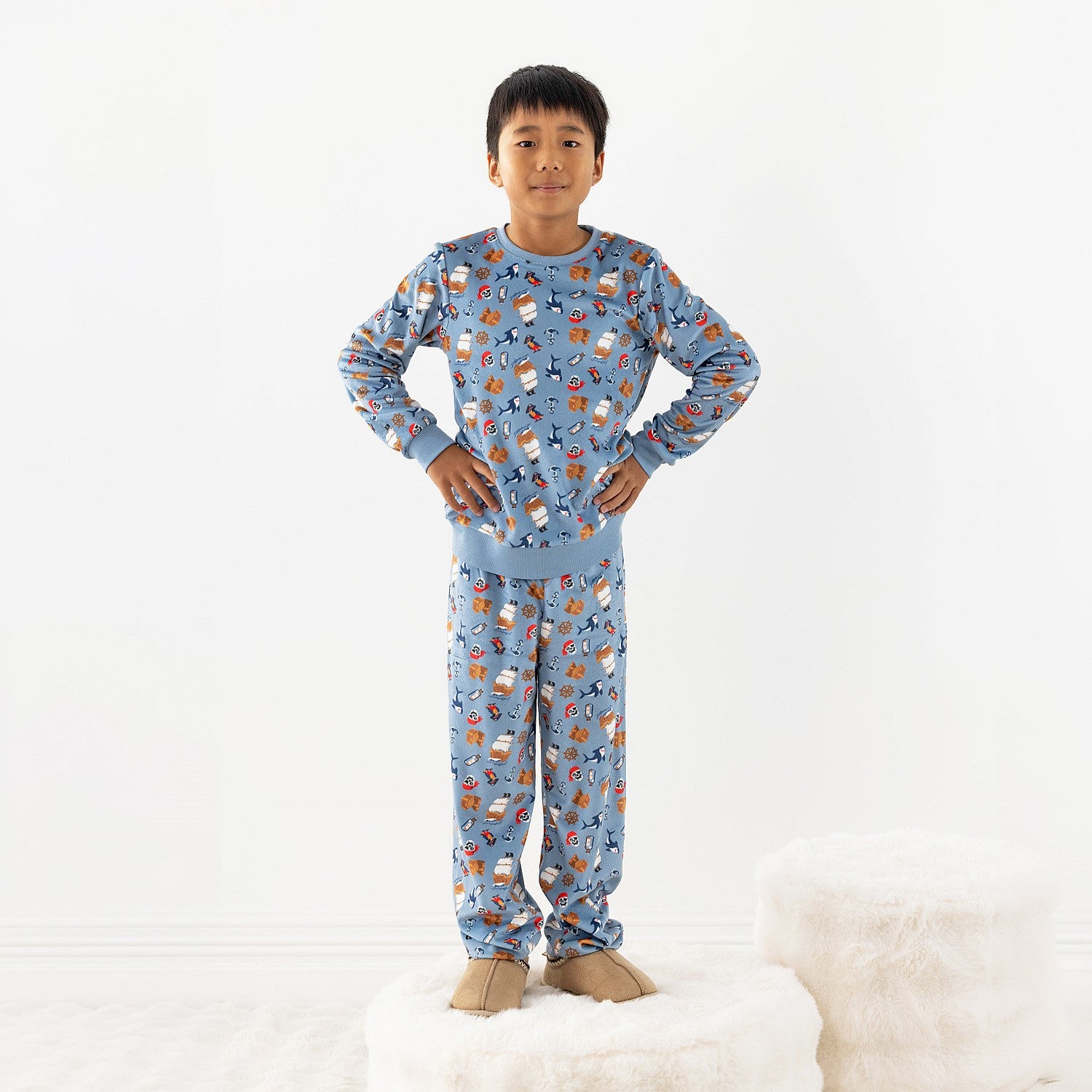 Child wearing blue pirate printed pyjamas standing on a stool on a white rug.