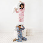 Two children wearing printed pyjama sets, one blue and one pink, together on a white rug.