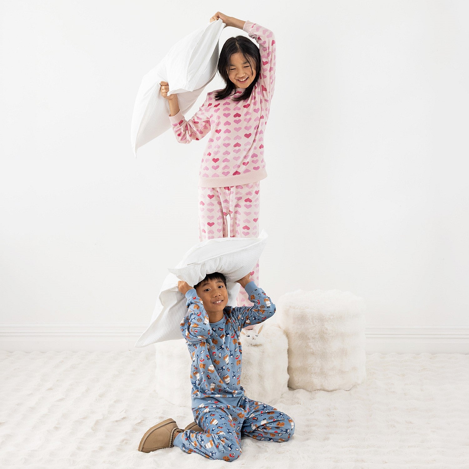 Two children wearing printed pyjama sets, one blue and one pink, together on a white rug.