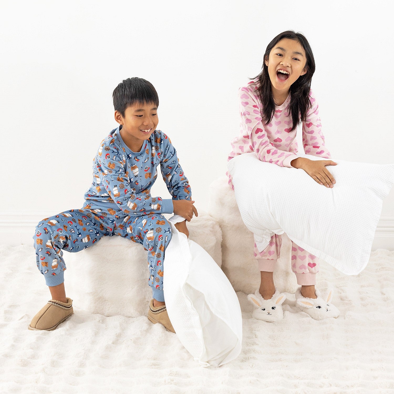 Two children wearing printed pyjama sets, one blue and one pink, sitting together on a white rug.