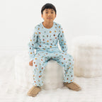 Child wearing light blue space printed pyjamas sitting on a stool on a white background.