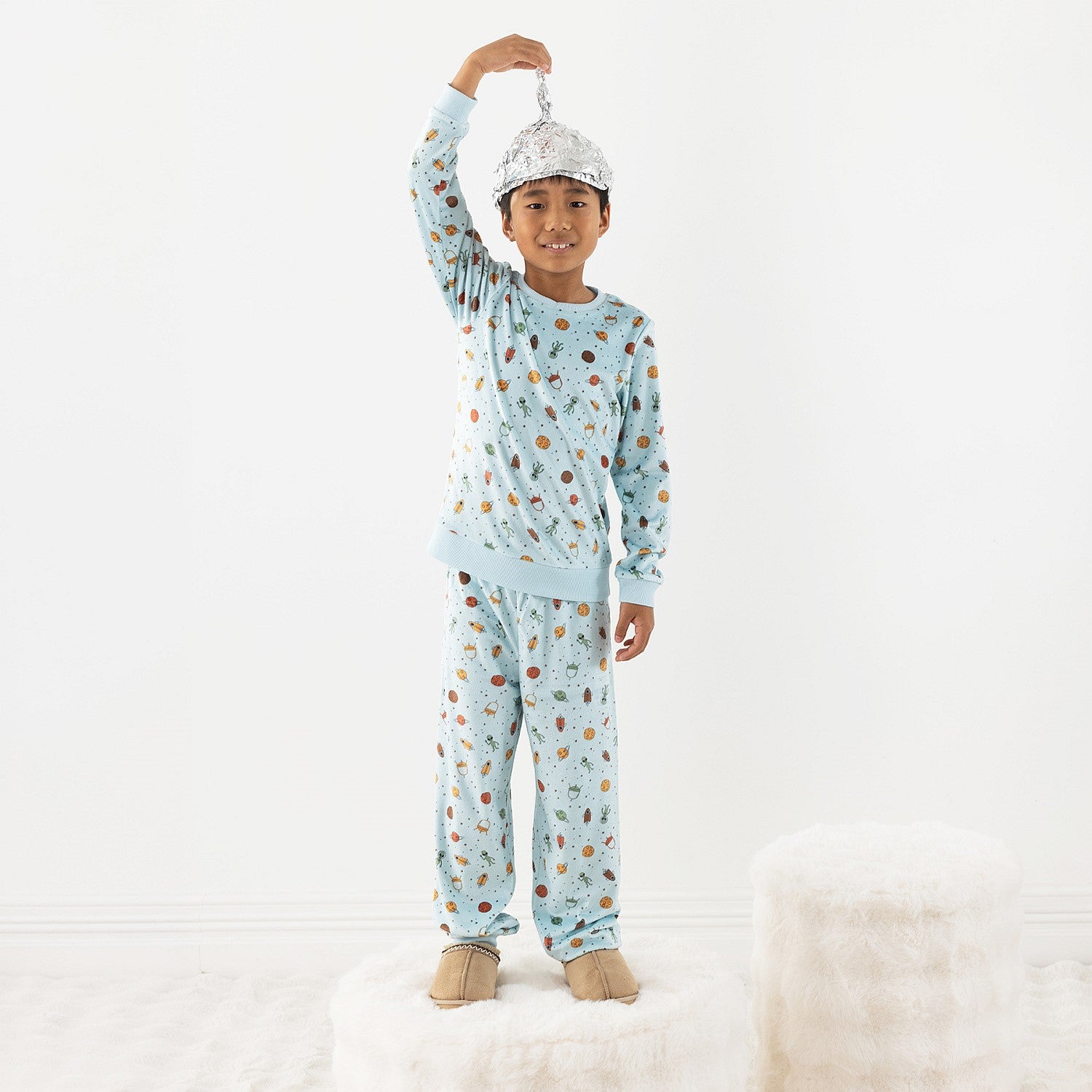 Child wearing light blue space printed pyjamas on a white background.