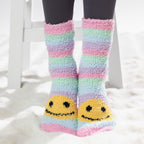 Colourful kids bed socks with yellow smiley face design, worn on a soft white rug.