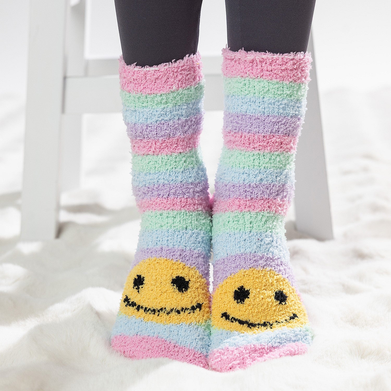Colourful kids bed socks with yellow smiley face design, worn on a soft white rug.