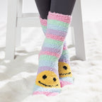 Colourful kids bed socks with yellow smiley face design, worn on a soft white rug.