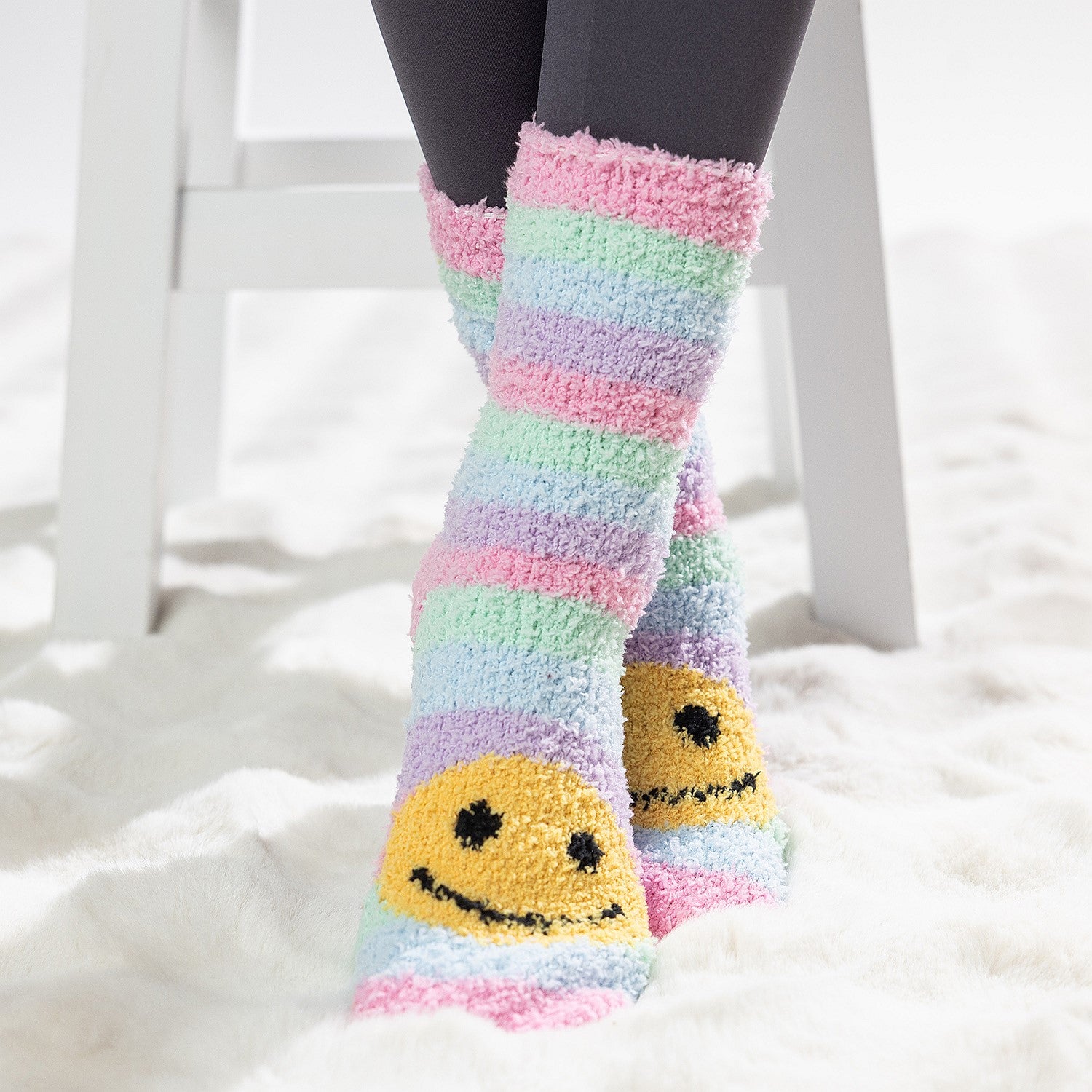 Colourful kids bed socks with yellow smiley face design, worn on a soft white rug.