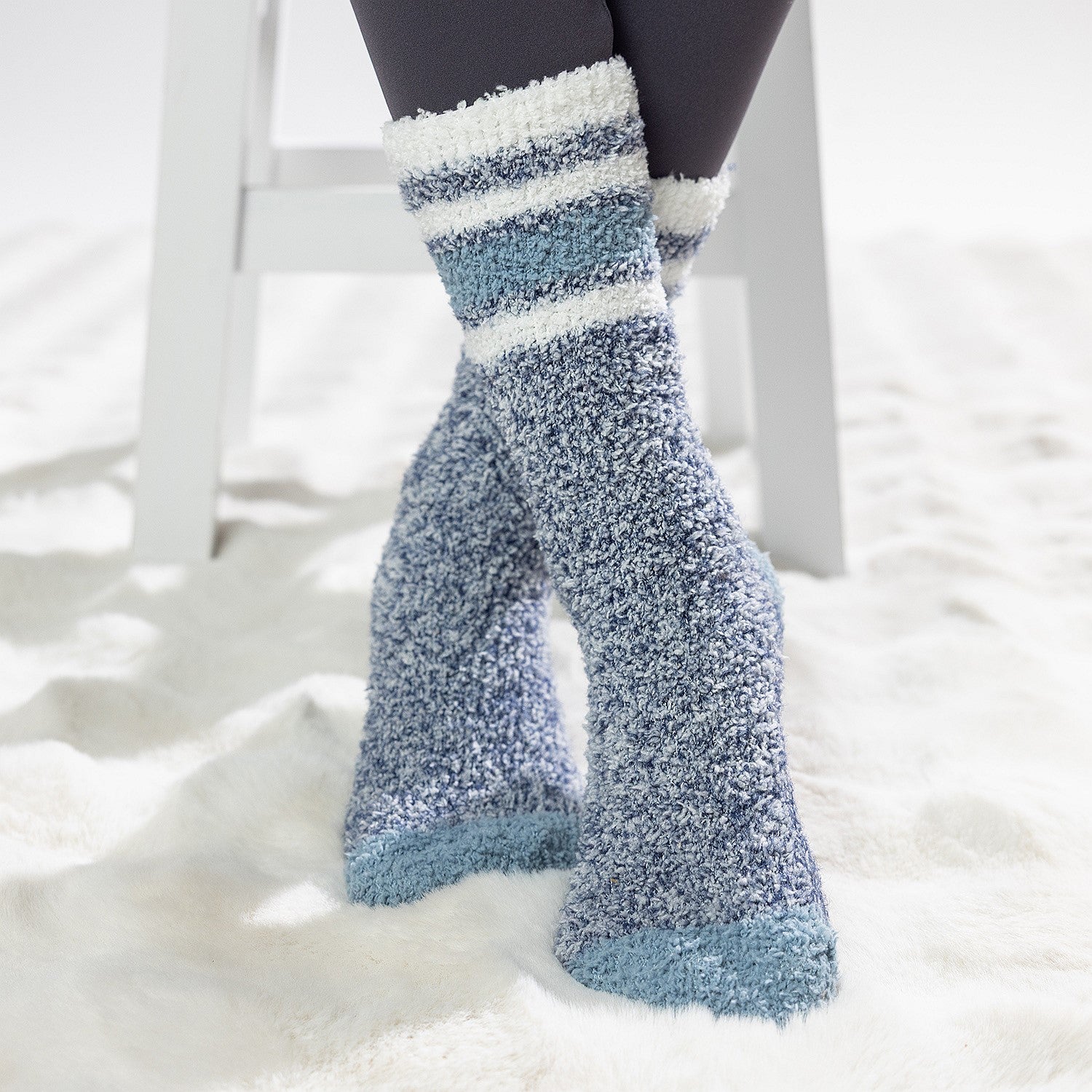 Blue sherpa lined slipper socks with striped cuff detail, worn on a soft white rug.