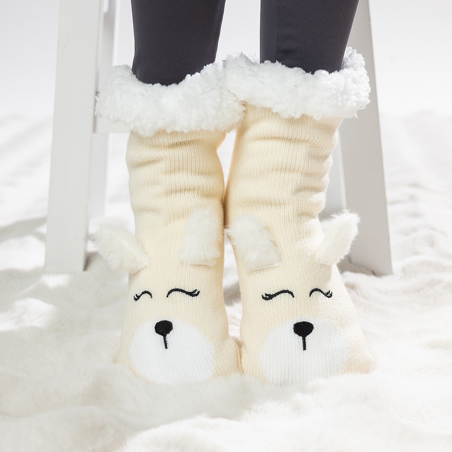 Cream puppy slipper socks with soft fleece lining worn on a white rug.