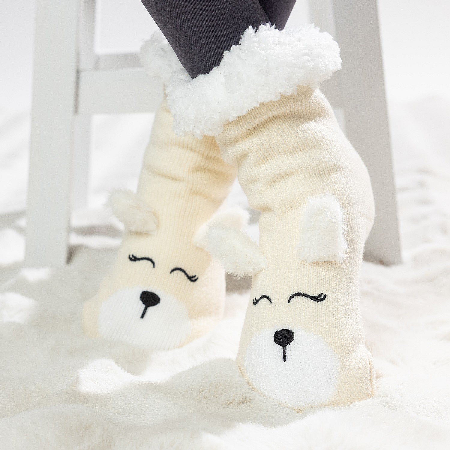 Cream puppy slipper socks with soft fleece lining worn on a white rug.
