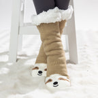 Brown sloth slipper socks with sherpa lining and cute face design, worn on a soft white rug.