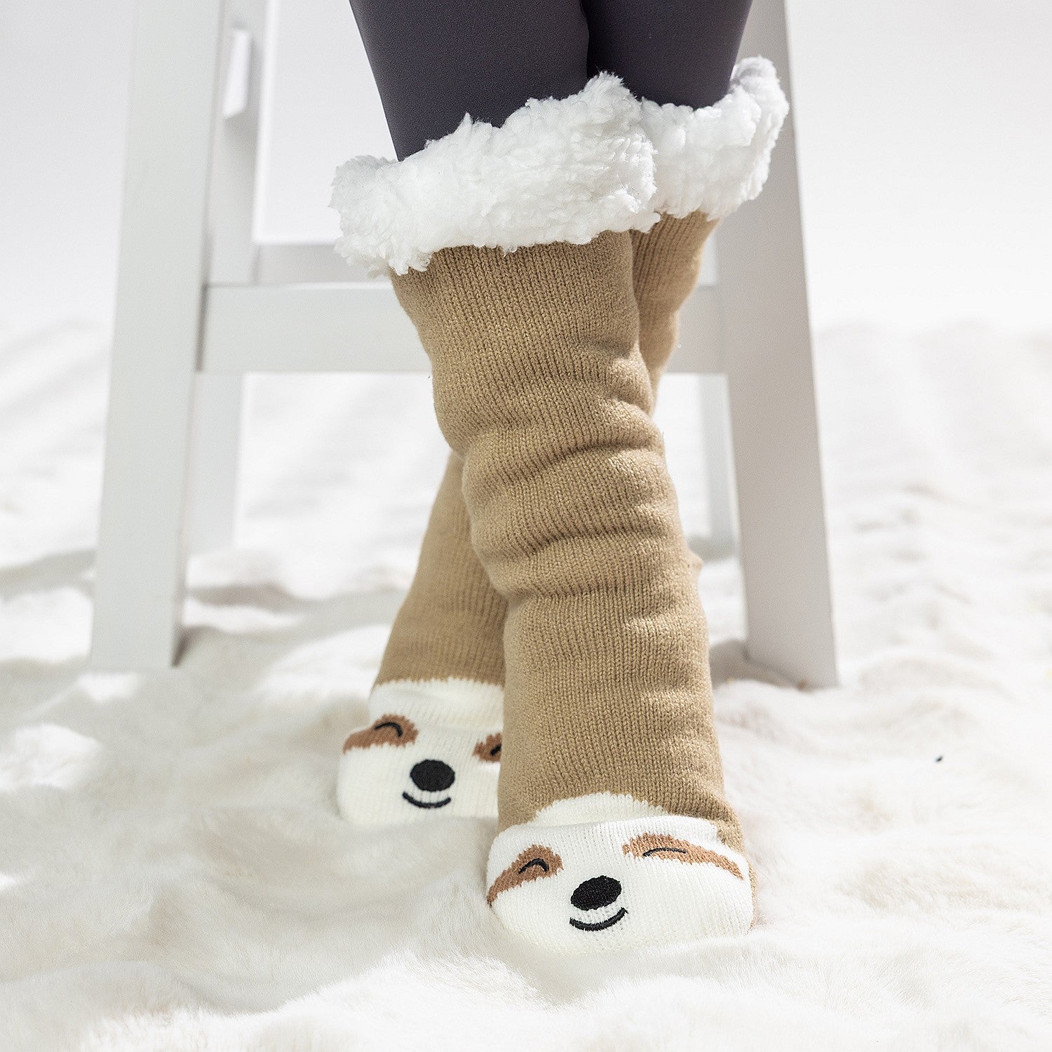Brown sloth slipper socks with sherpa lining and cute face design, worn on a soft white rug.