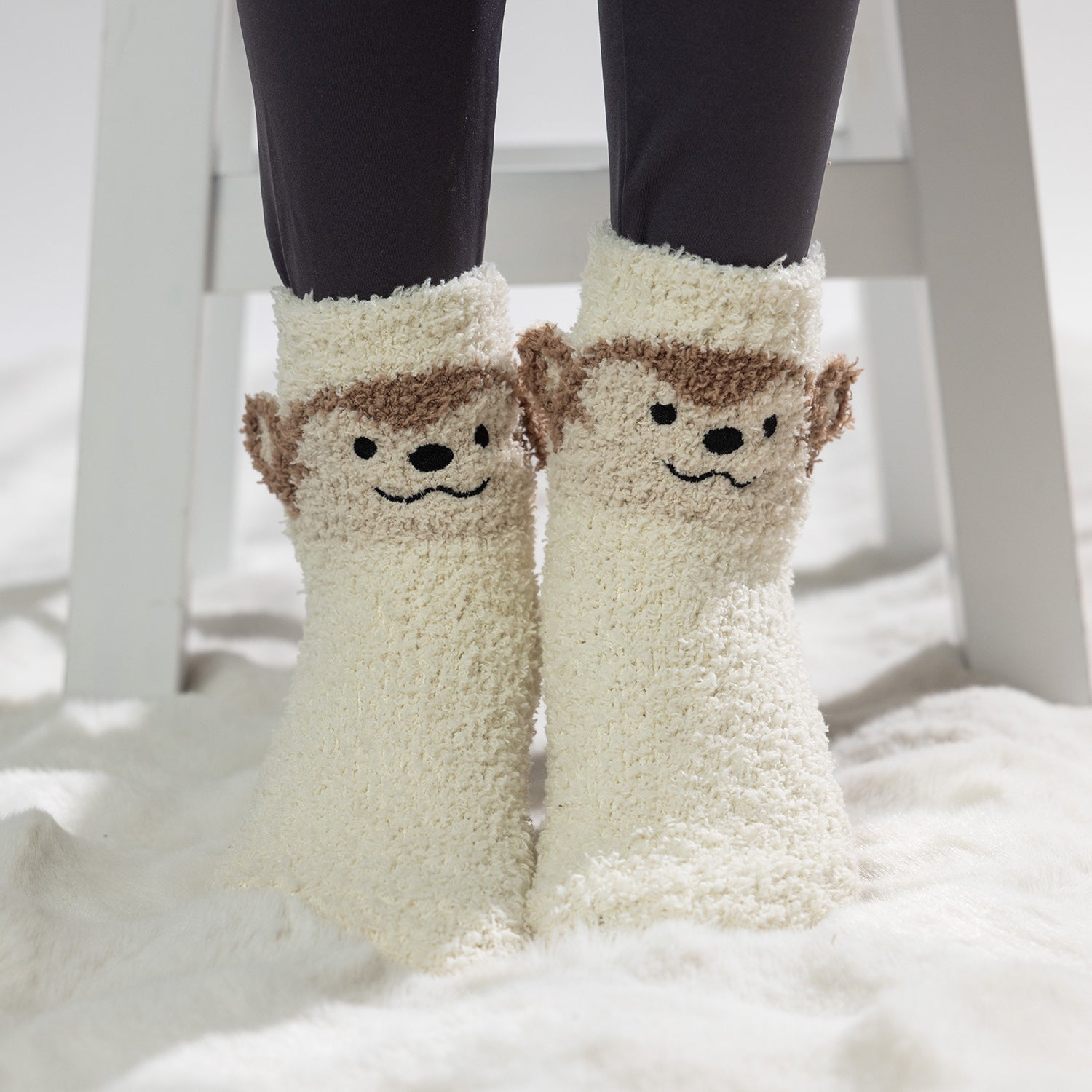 Cream kids bed socks with cute monkey face design, worn on a soft white rug.
