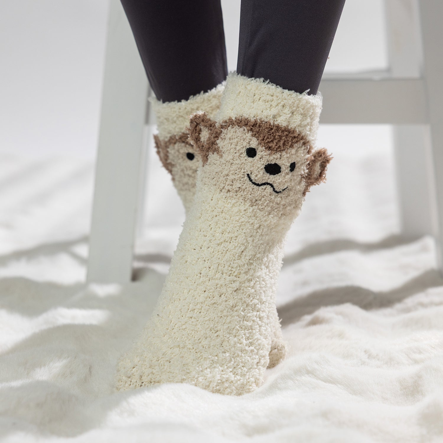 Cream kids bed socks with cute monkey face design, worn on a soft white rug.