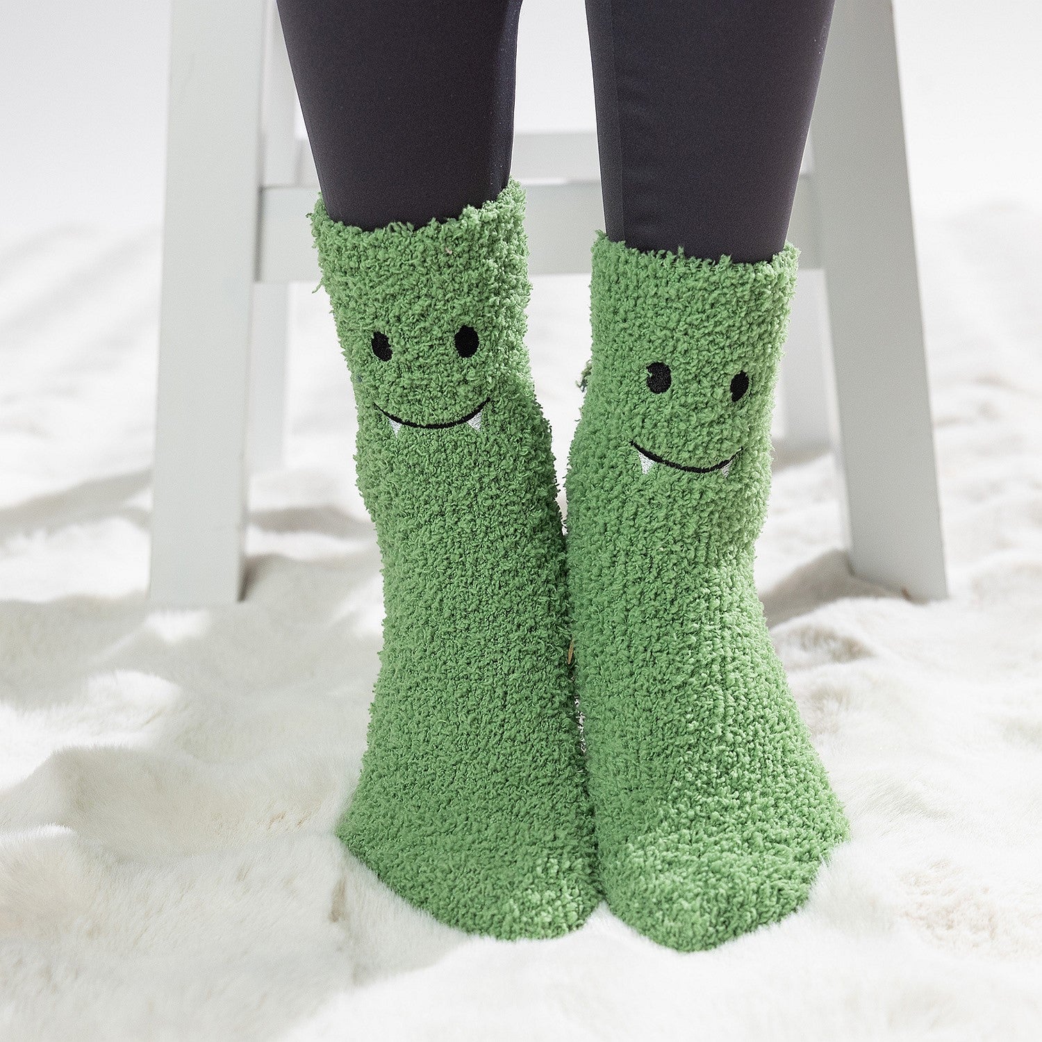 Green kids bed socks with smiling frog face design, worn on a soft white rug.