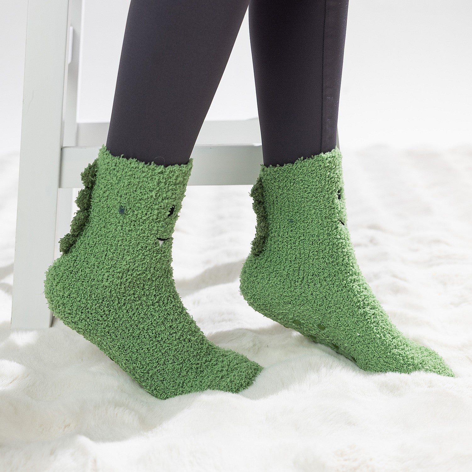 Green kids bed socks with smiling frog face design, worn on a soft white rug.
