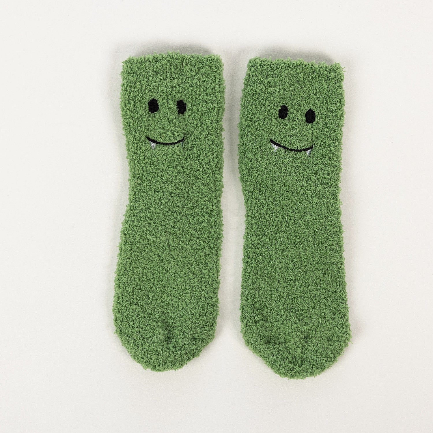 Green kids bed socks with smiling frog face design, worn on a soft white rug.