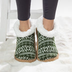Green Nordic slipper socks with white fleece lining worn on a soft white rug.