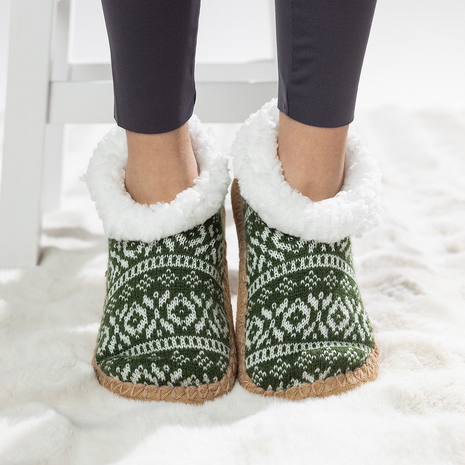 Green Nordic slipper socks with white fleece lining worn on a soft white rug.