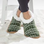 Green Nordic slipper socks with white fleece lining worn on a soft white rug.