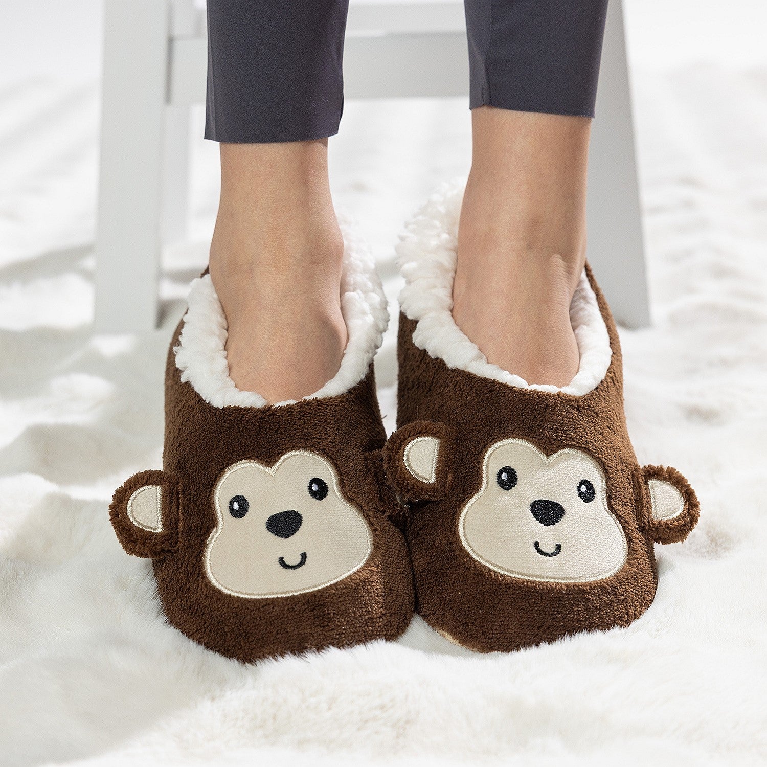 Brown monkey slipper socks with soft fleece lining worn on a white rug.
