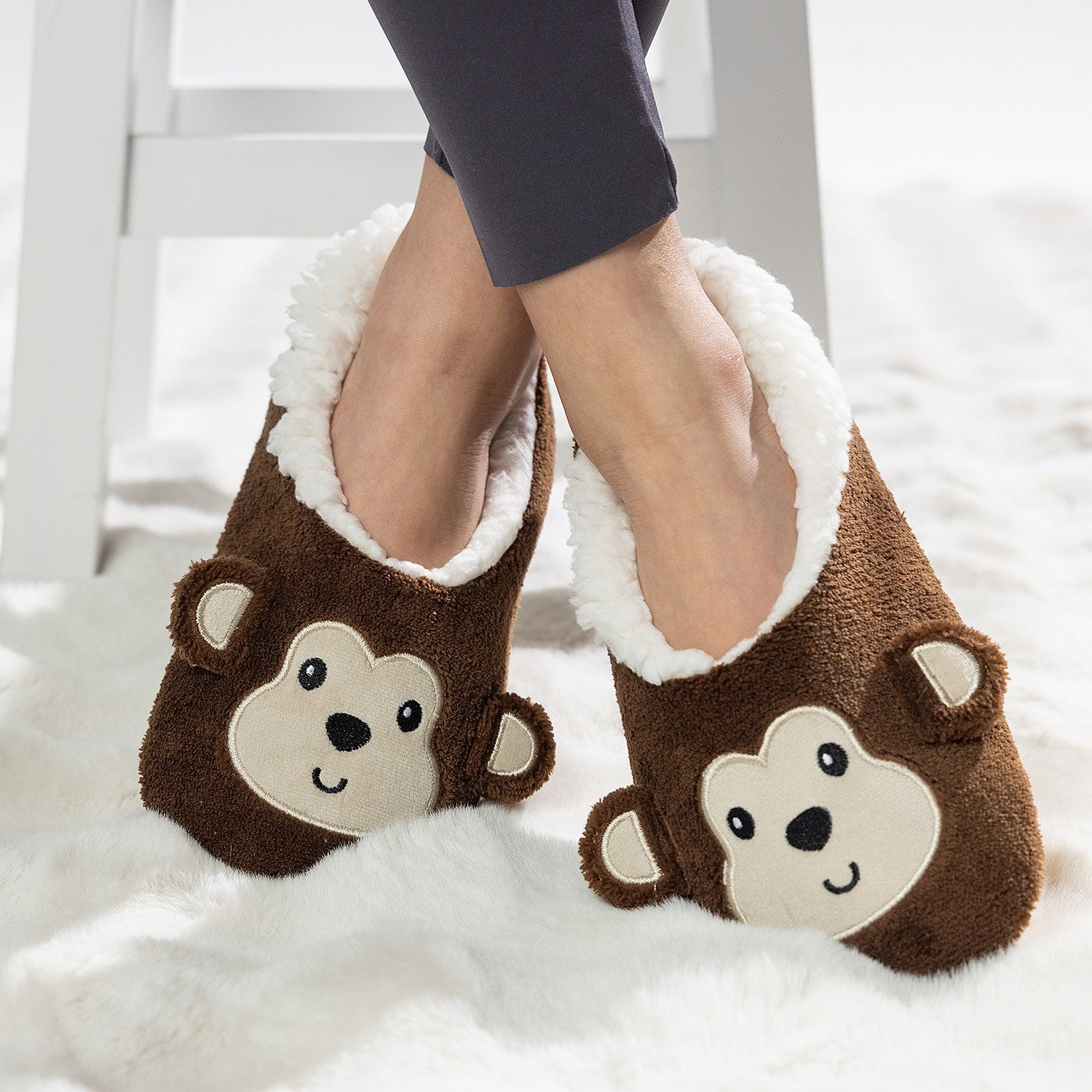 Brown monkey slipper socks with soft fleece lining worn on a white rug.
