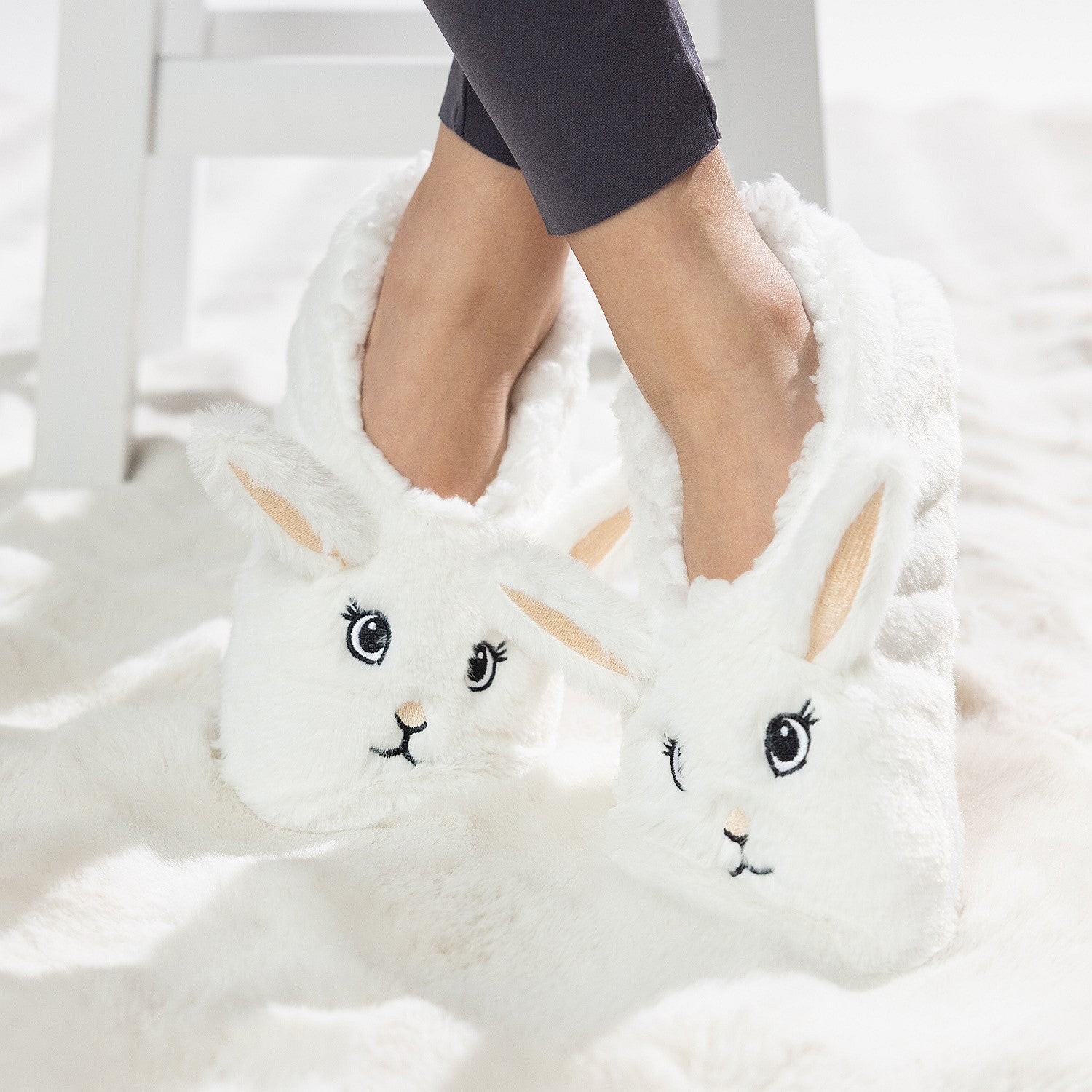 White bunny slipper socks with fleece lining worn on a soft white rug.