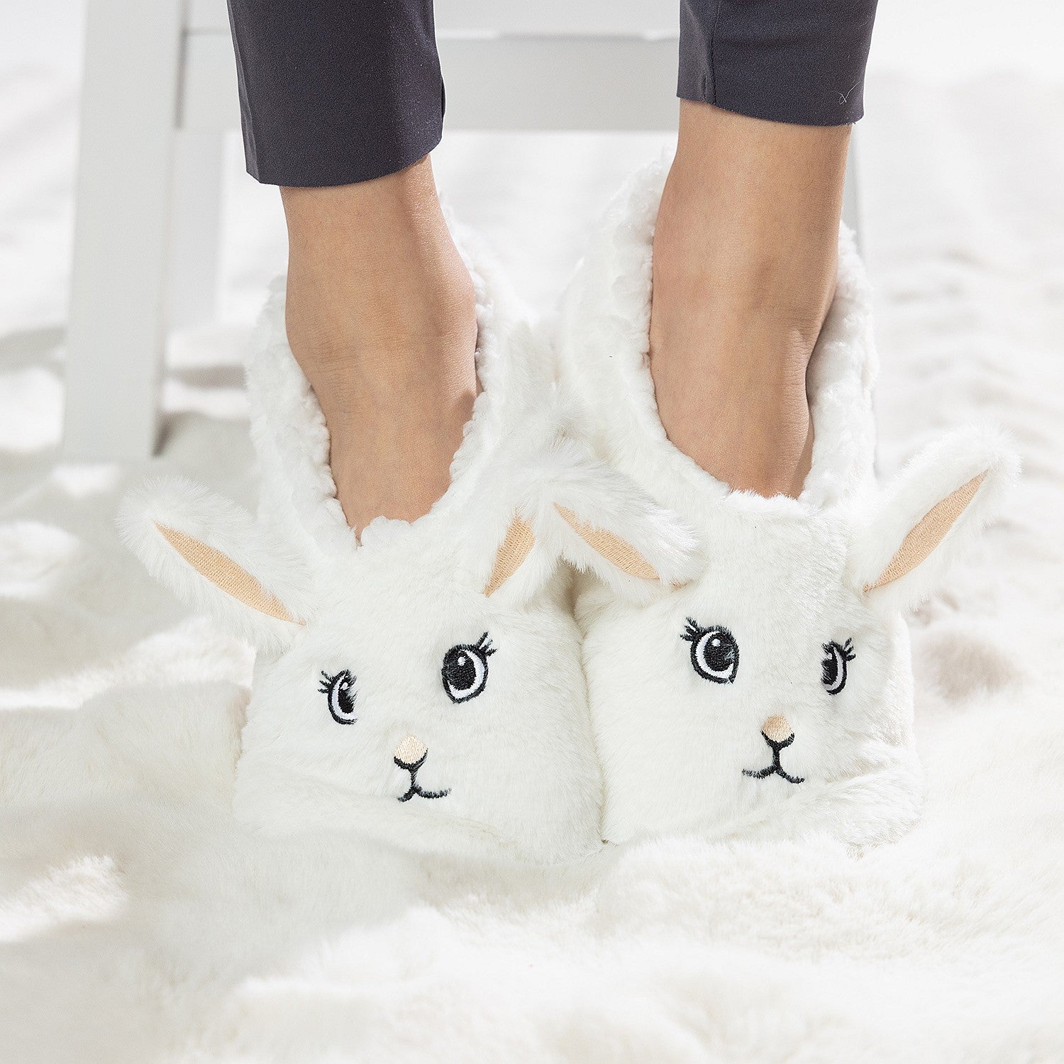 White bunny slipper socks with fleece lining worn on a soft white rug.