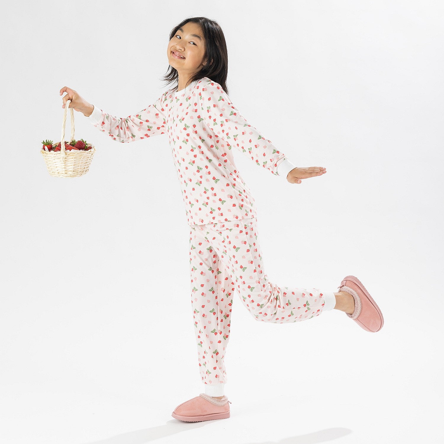 Child wearing pink and red heart print pyjamas posing on a white background.