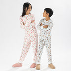 Two children wearing printed pyjama sets, one in pink hearts and one in blue dog stripe print, posing back to back.