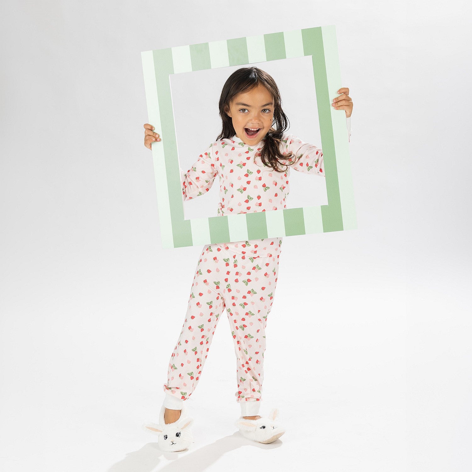 Child wearing pink and red heart print pyjamas posing on a white background.