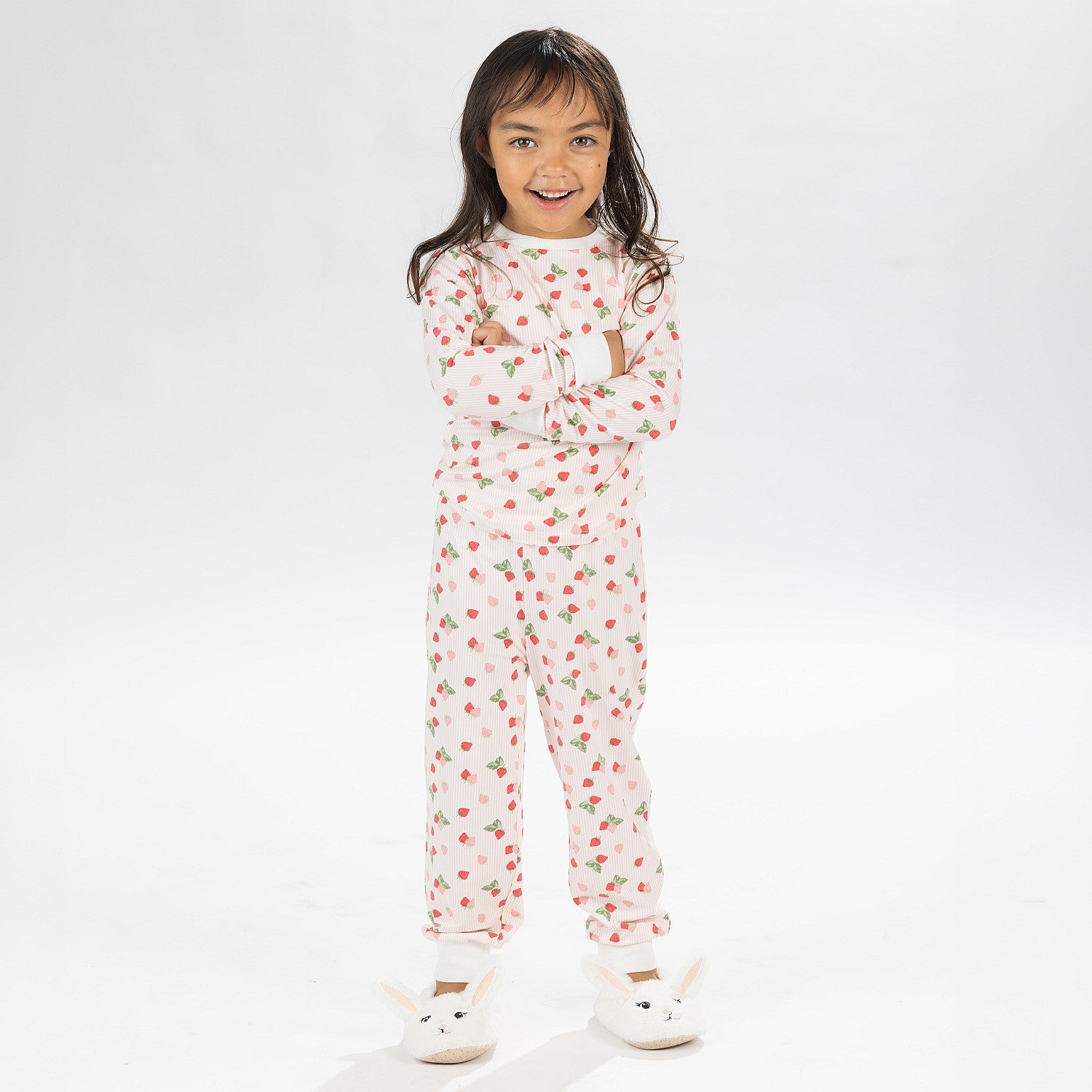 Child wearing pink and red heart print pyjamas posing on a white background.