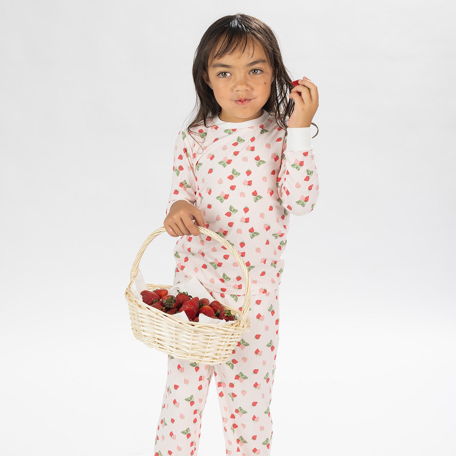 Child wearing pink and red heart print pyjamas posing on a white background.