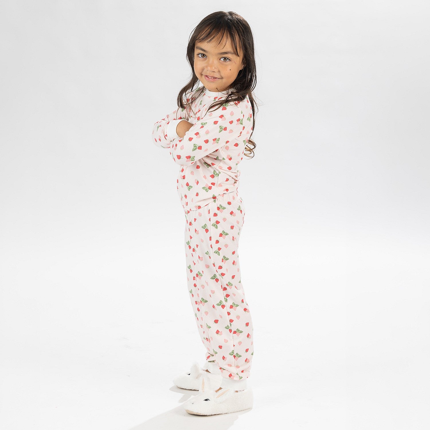 Child wearing pink and red heart print pyjamas posing on a white background.