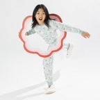 Child wearing a light green printed pyjama set with unicorns on a white background. Wearing bunny slippers.