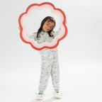 Child wearing a light green printed pyjama set with unicorns on a white background. Wearing bunny slippers.